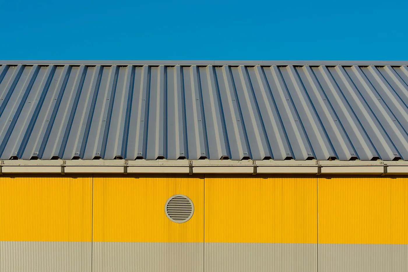 Gray corrugated metal roof panels on an industrial building with a yellow metal wall