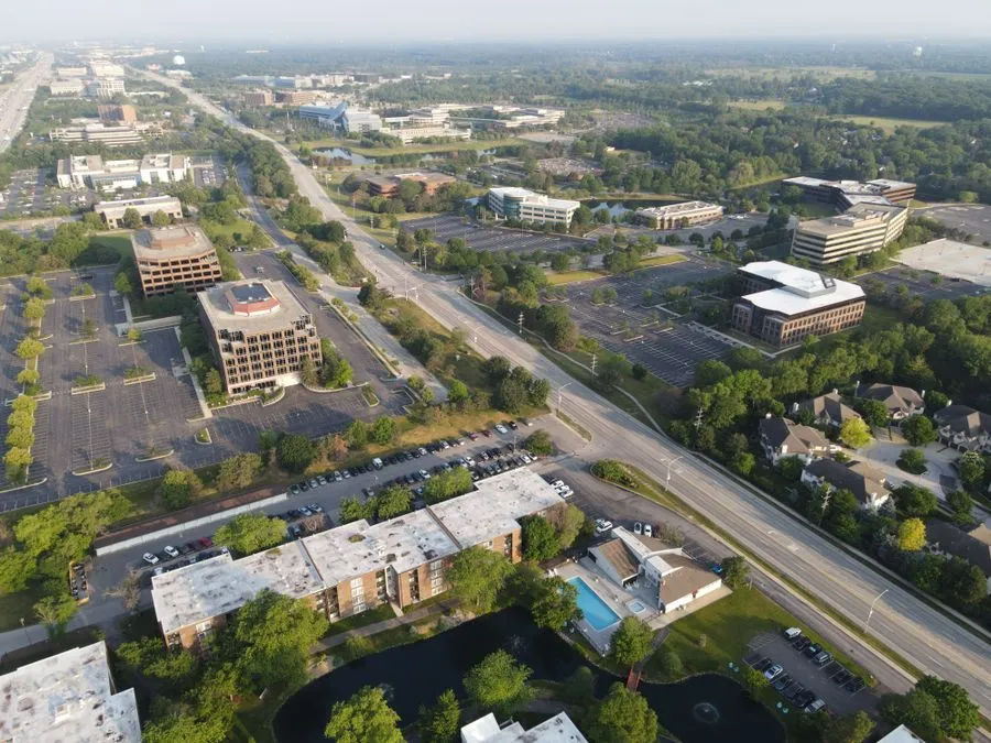 Aerial view of low-rise office buildings with flat roofs, parking lots, and a pond in a suburban office park